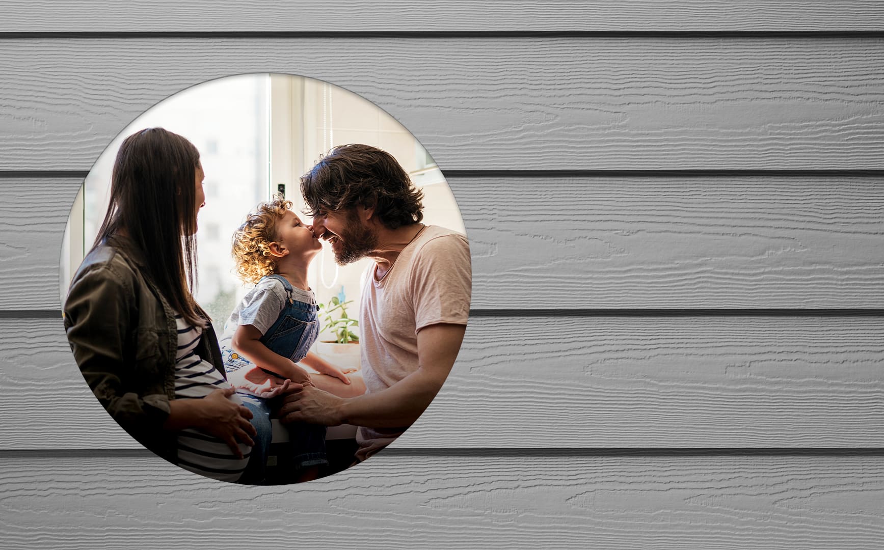 A family smiles as a child kisses their father's nose.