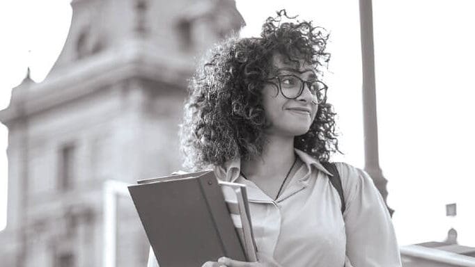A woman standing in front of a university building holding a notebook