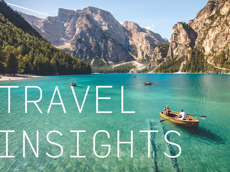 Kayakers in a clear lake surrounded by a mountain range with the caption "Travel Insights".