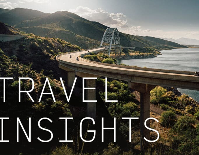 Motorcyclists traveling on a bridge over green rolling hills with the caption "Travel Insights"
