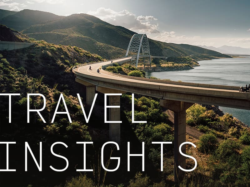 Motorcyclists traveling on a bridge over green rolling hills with the caption "Travel Insights"